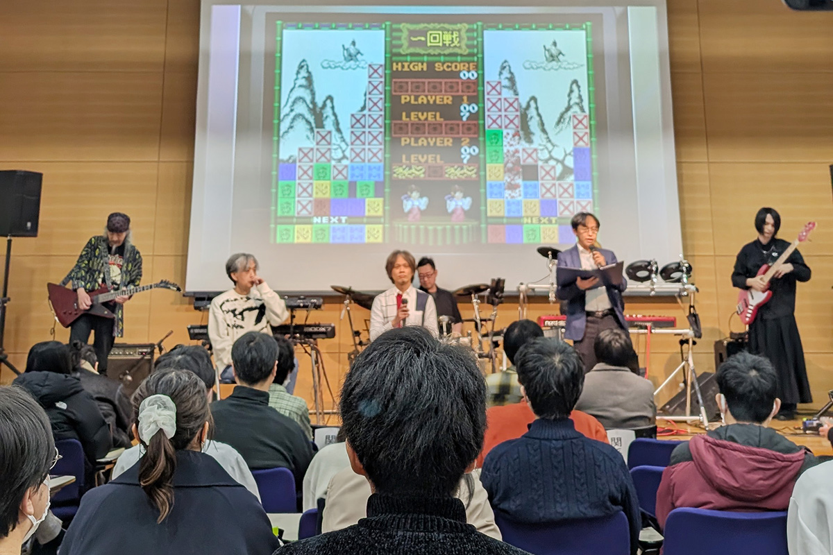「ゲームオーディオ研究の過去・現在・未来」シンポジウムの壇上の様子を観客側から見ている
